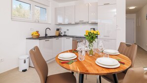 A modern kitchen with white cabinets, a dining table set for four, and a vase with yellow flowers. - Moderne Ferienwohnung mit Meerblick, überdachter Terrasse & Whirlpool (Dramalj)