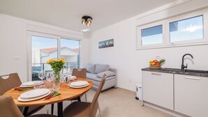 A modern kitchen with white cabinets, a dining table set for four, and a gray sofa in the background. - Moderne Ferienwohnung mit Meerblick, überdachter Terrasse & Whirlpool (Dramalj)