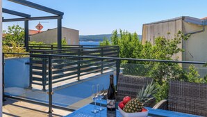 A rooftop terrace with a table set for two, a bottle of wine, and a bowl of fruit. - Moderne Ferienwohnung mit Meerblick, überdachter Terrasse & Whirlpool (Dramalj)