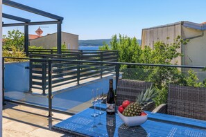 A rooftop terrace with a table set for two, a bottle of wine, and a bowl of fruit. - Moderne Ferienwohnung mit Meerblick, überdachter Terrasse & Whirlpool (Dramalj)