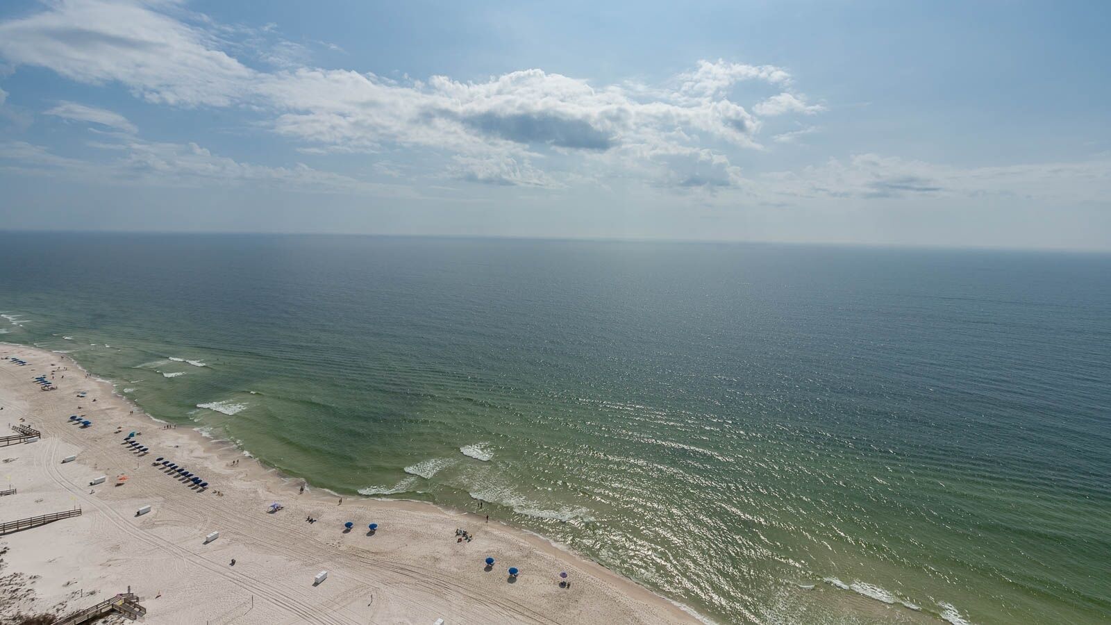 A beach with a clear view of the ocean, a sandy shore, and a few umbrellas.