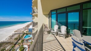 Een balkon met stoelen en een tafel, met uitzicht op een strand en een zwembad.