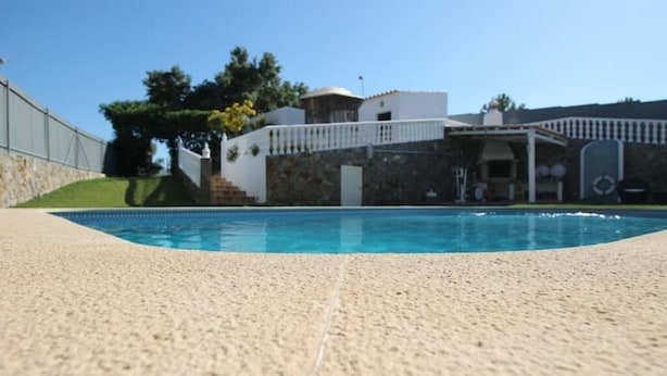 A swimming pool with a stone deck, a white building with a balcony, and a stone wall. - Rural Villa with Private Pool near Vilamoura (Quarteira)