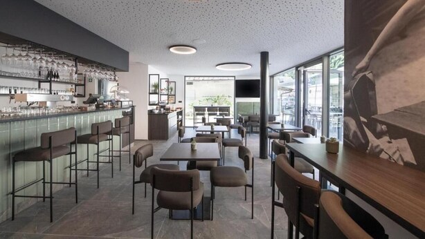 Un interior de restaurante moderno con asientos de bar, mesas y un ventanal con vistas.