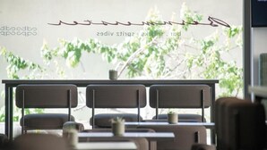 Interior de un restaurante con diseño moderno, que presenta una mesa larga con sillas, una lámpara colgante y vistas a zonas verdes al exterior.