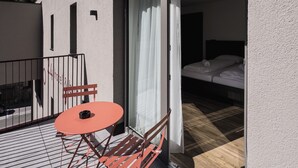 Una habitación de hotel con cama, un balcón pequeño con mesa y sillas, y vista al bosque.