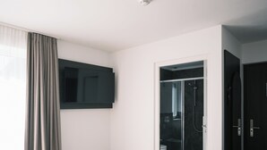 Habitación de hotel con cama, televisión, zona de ducha y puerta.