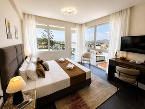 A hotel room with a large bed, a desk with a TV, a chair, and a balcony with a view of the city. - Amaris Hotel & Spa by Athens Prime Hotels (Athens)