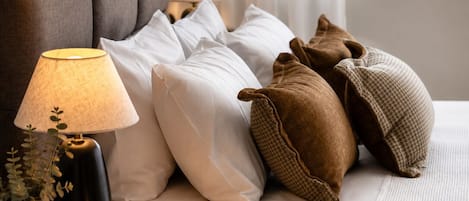 A neatly made bed with white and brown pillows, a bedside lamp, and a candle on a marble nightstand.