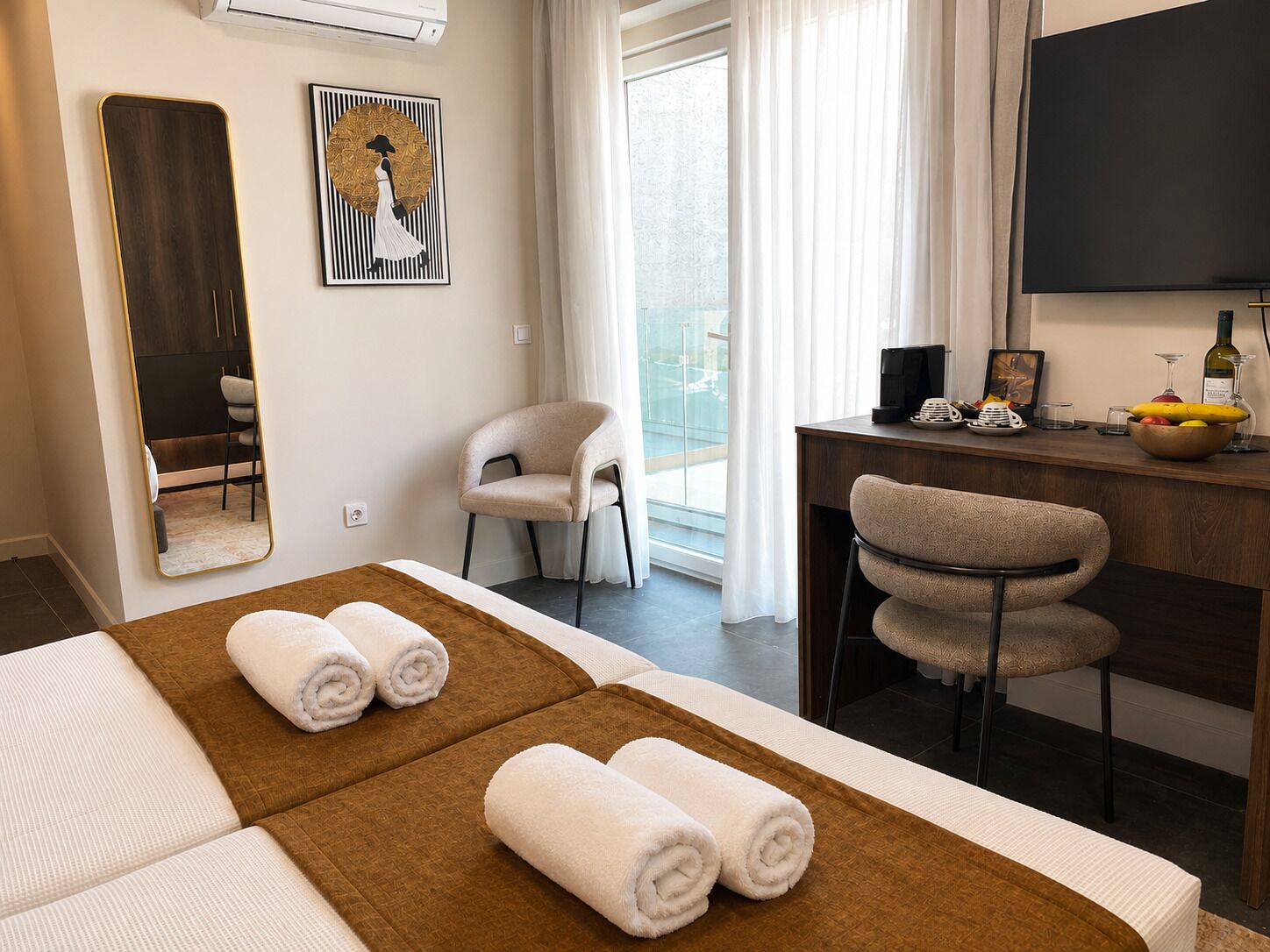 A hotel room with a bed, a desk with a computer, a chair, a large mirror, and a painting on the wall.