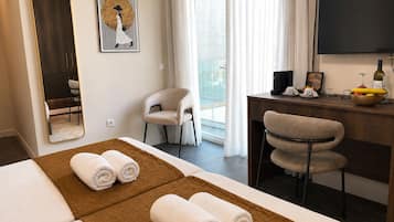 A hotel room with a bed, a desk with a computer, a chair, a large mirror, and a painting on the wall.
