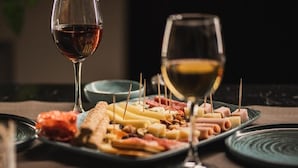 A charcuterie board with various cheeses, meats, and crackers, accompanied by two glasses of wine. - Amaris Hotel & Spa by Athens Prime Hotels (Athens)