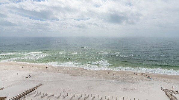 Uma praia com areal, ondas e céu nublado.