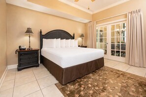 Un dormitorio de hotel con una cama grande, un aparador, dos lámparas de noche, una alfombra floral y una puerta corrediza de cristal al exterior.