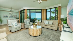 A living room with a large window, a ceiling fan, and a round coffee table. - Phoenix West 205 3 Bedroom Condo (Orange Beach)