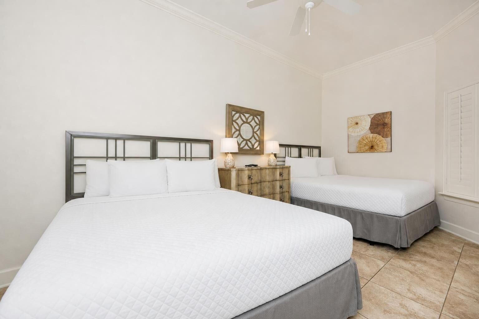 Une chambre d’hôtel avec deux lits, une table de chevet, une lampe et un ventilateur de plafond.