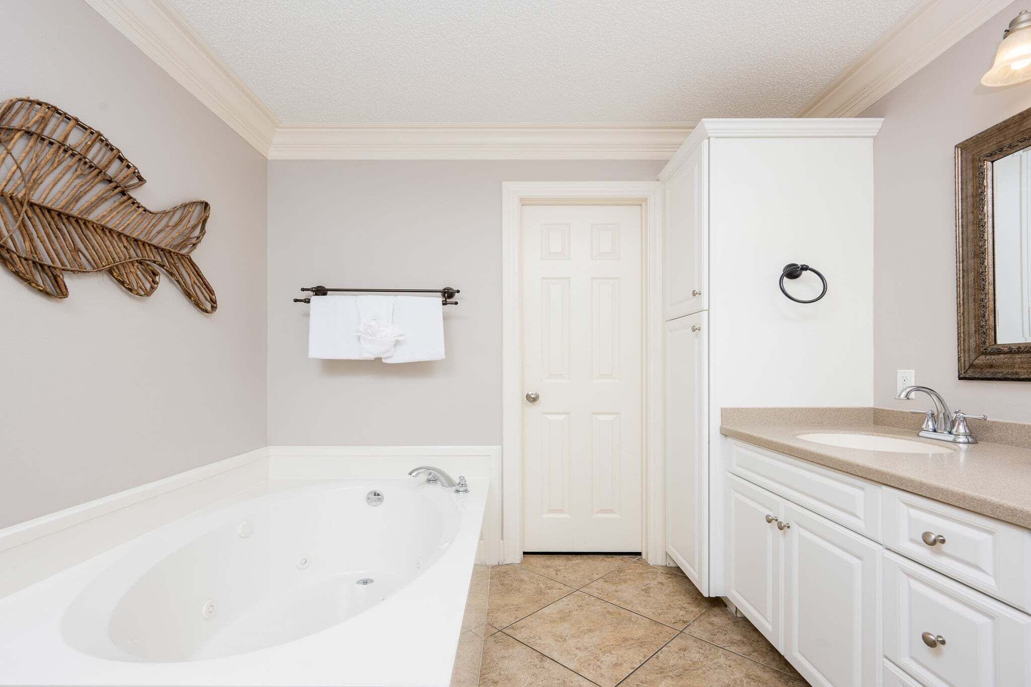 Un baño con una bañera grande, una puerta blanca, un tocador con lavabo y una decoración de pez montada en la pared.