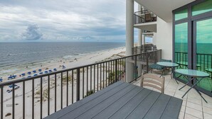 A balcony with a view of the beach, a table, and chairs. - The Oasis 606 Formerly Phoenix West Ii 606 3 Bedroom Condo (Orange Beach)