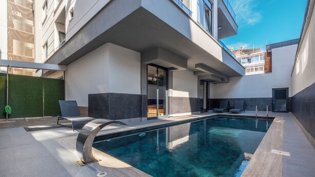 A modern outdoor pool area with a clear pool, lounge chairs, and a covered seating area.