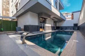 A modern outdoor pool area with a clear pool, lounge chairs, and a covered seating area.
