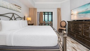A hotel room with a large bed, a television, a view of the sea, and a dining area with a table and chairs. - Phoenix West 1105 3 Bedroom Condo (Orange Beach)