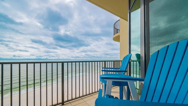 A balcony with a view of the beach and ocean, blue chairs, and a glass railing. - Phoenix West 1105 3 Bedroom Condo (Orange Beach)