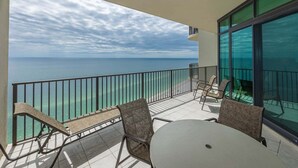A balcony with a view of the ocean, a table, and two chairs. - Phoenix West 2408 3 Bedroom Condo (Orange Beach)