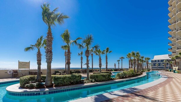 Una piscina con palme, cielo sereno e un edificio con balconi.