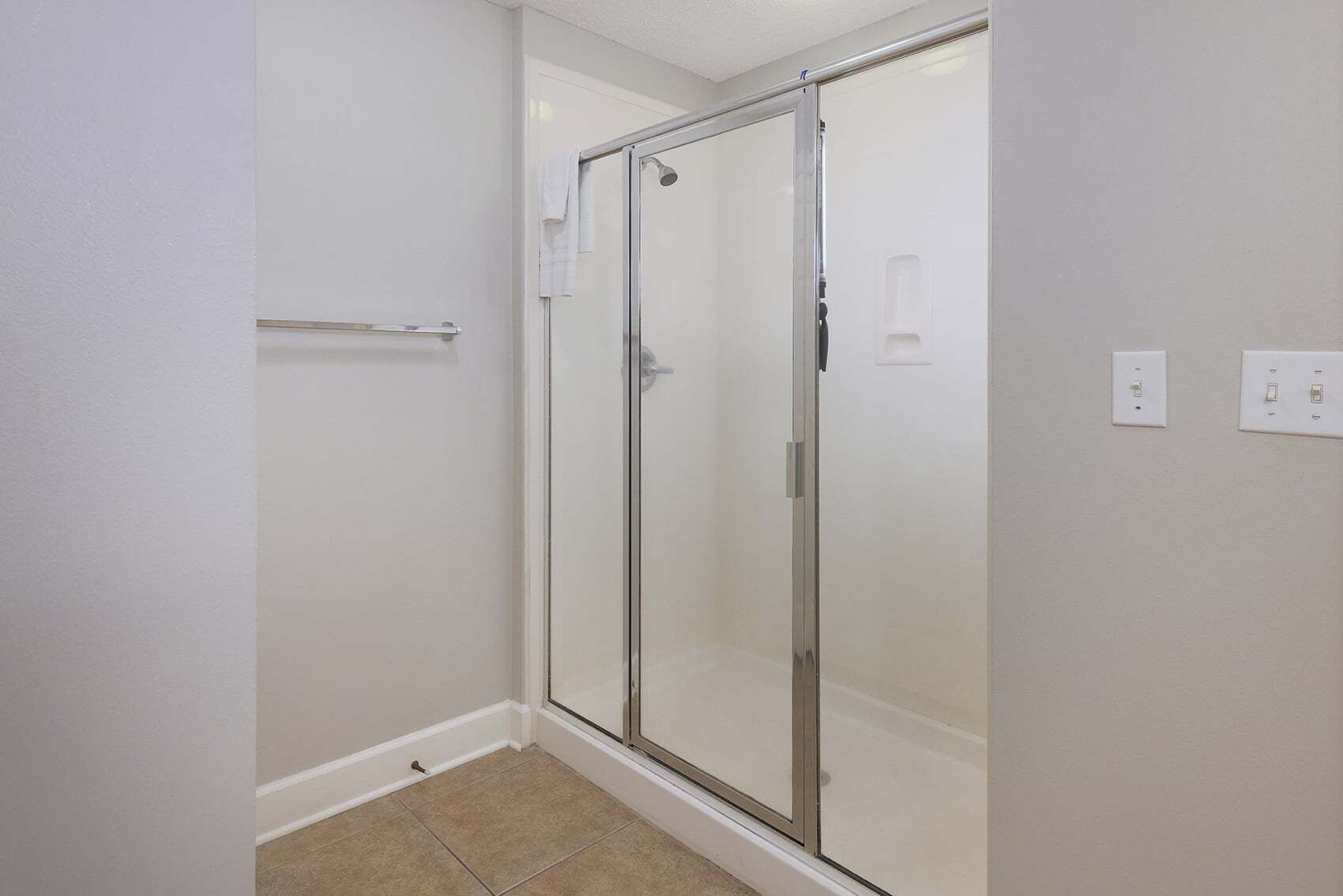 A bathroom with a glass shower enclosure, a towel rack, and a toilet paper holder.