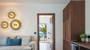 A modern living room with a sofa, decorative wall lights, and a view of the ocean through an open door. - Del Mare (Bali)