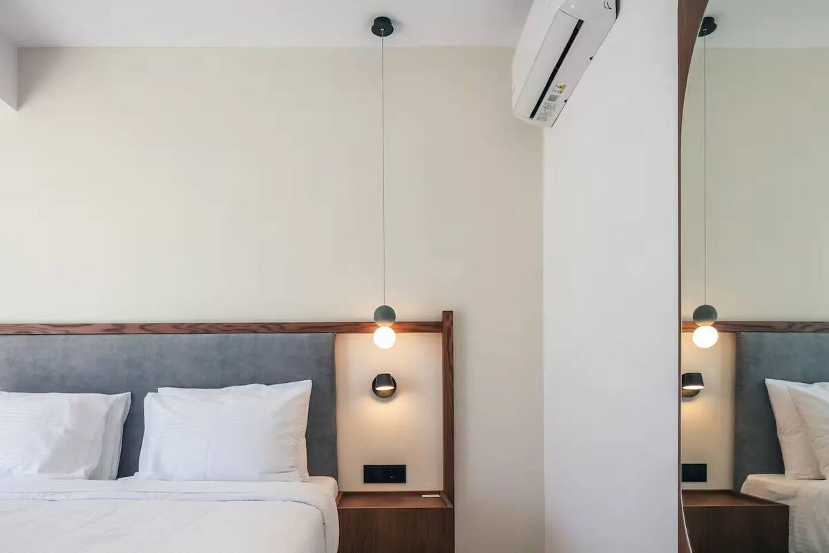 A hotel room with a bed, bedside tables, a mirror, and an air conditioning unit.