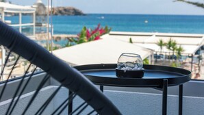 A balcony with a glass enclosure, a small table with a glass container, and a view of the ocean and distant buildings. - Del Mare (Bali)