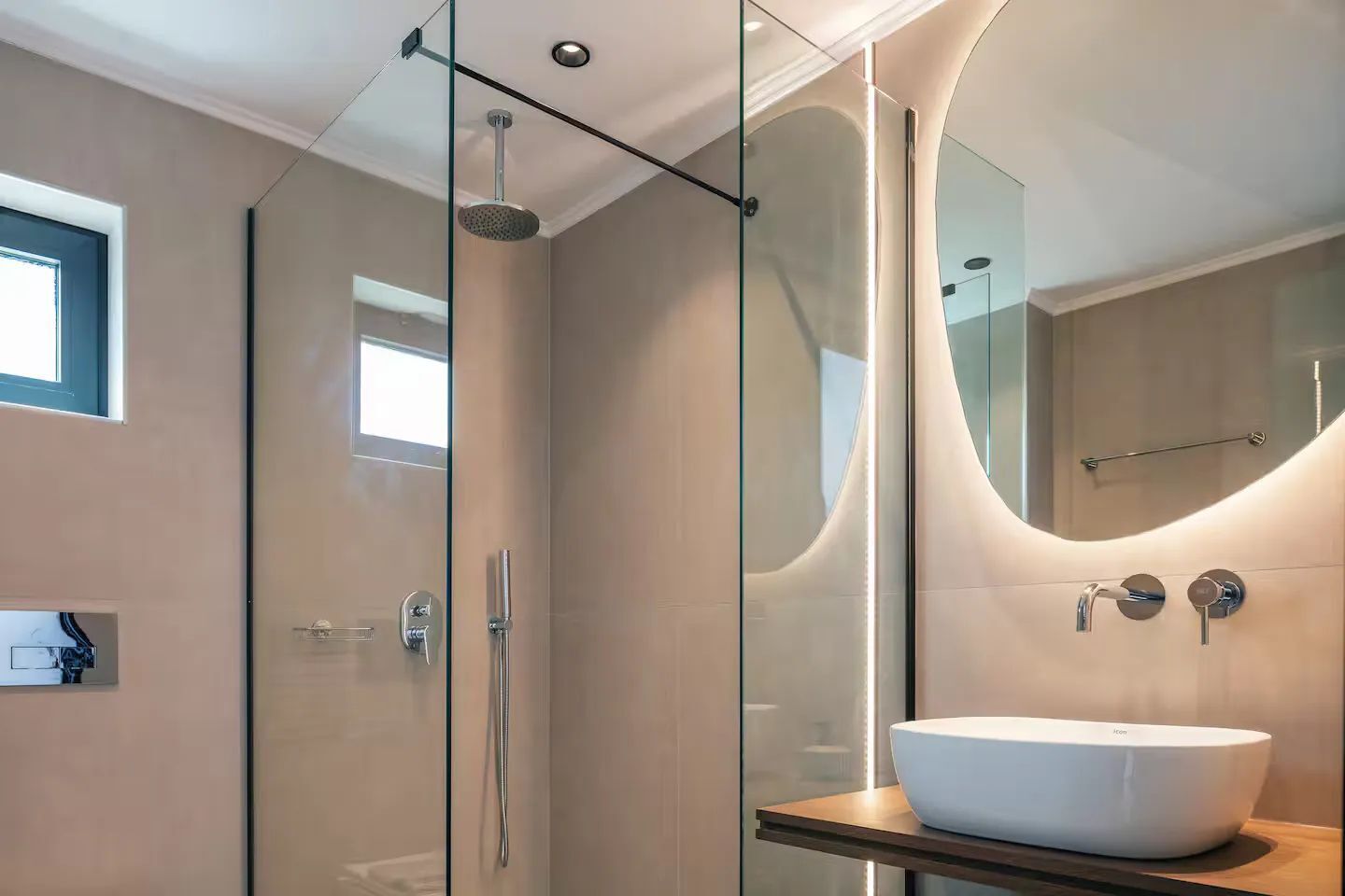 A modern bathroom with a glass-enclosed shower, a large mirror, and a white sink on a wooden countertop.