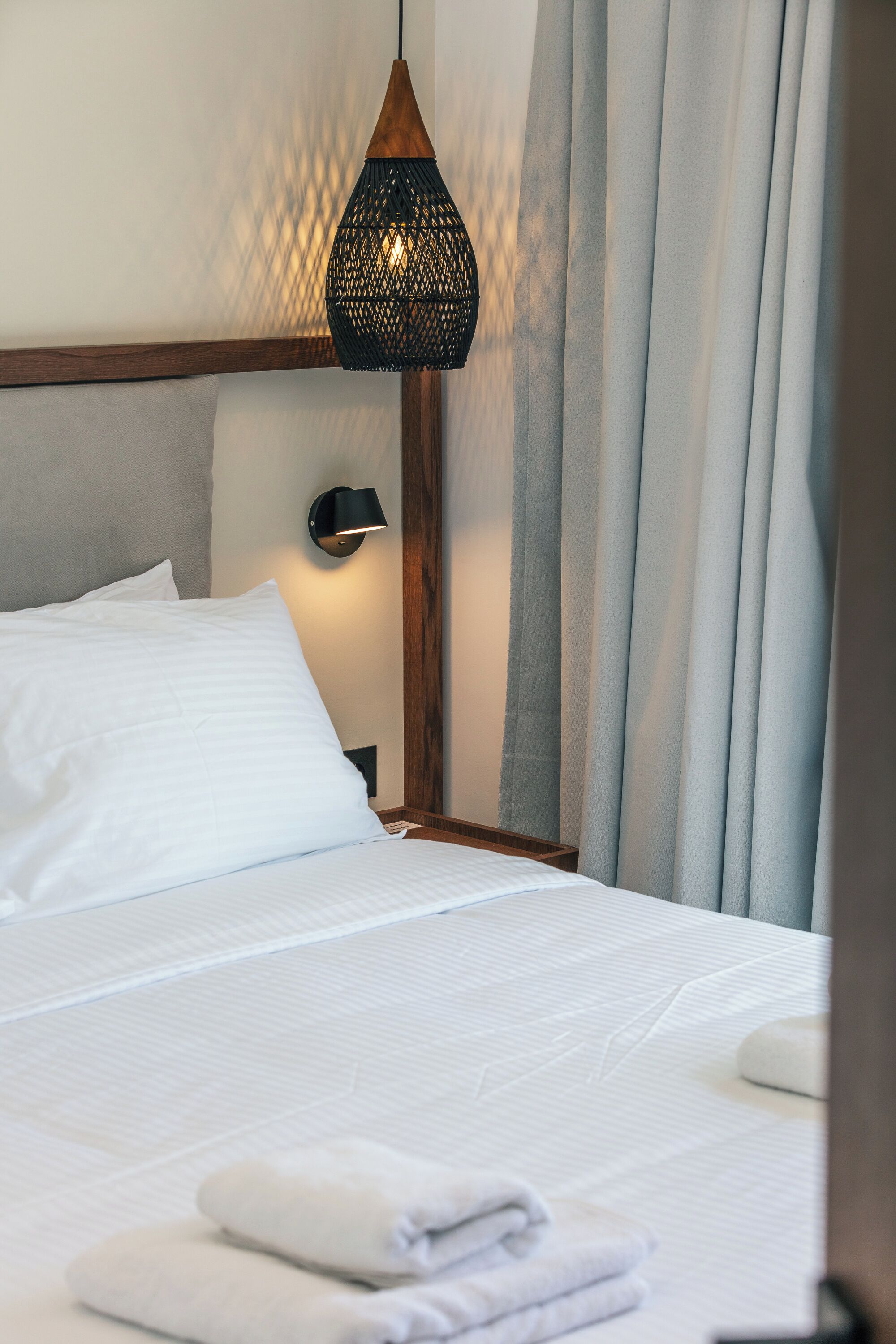 A neatly made bed with white linens, a black wall-mounted lamp, and a hanging light fixture.