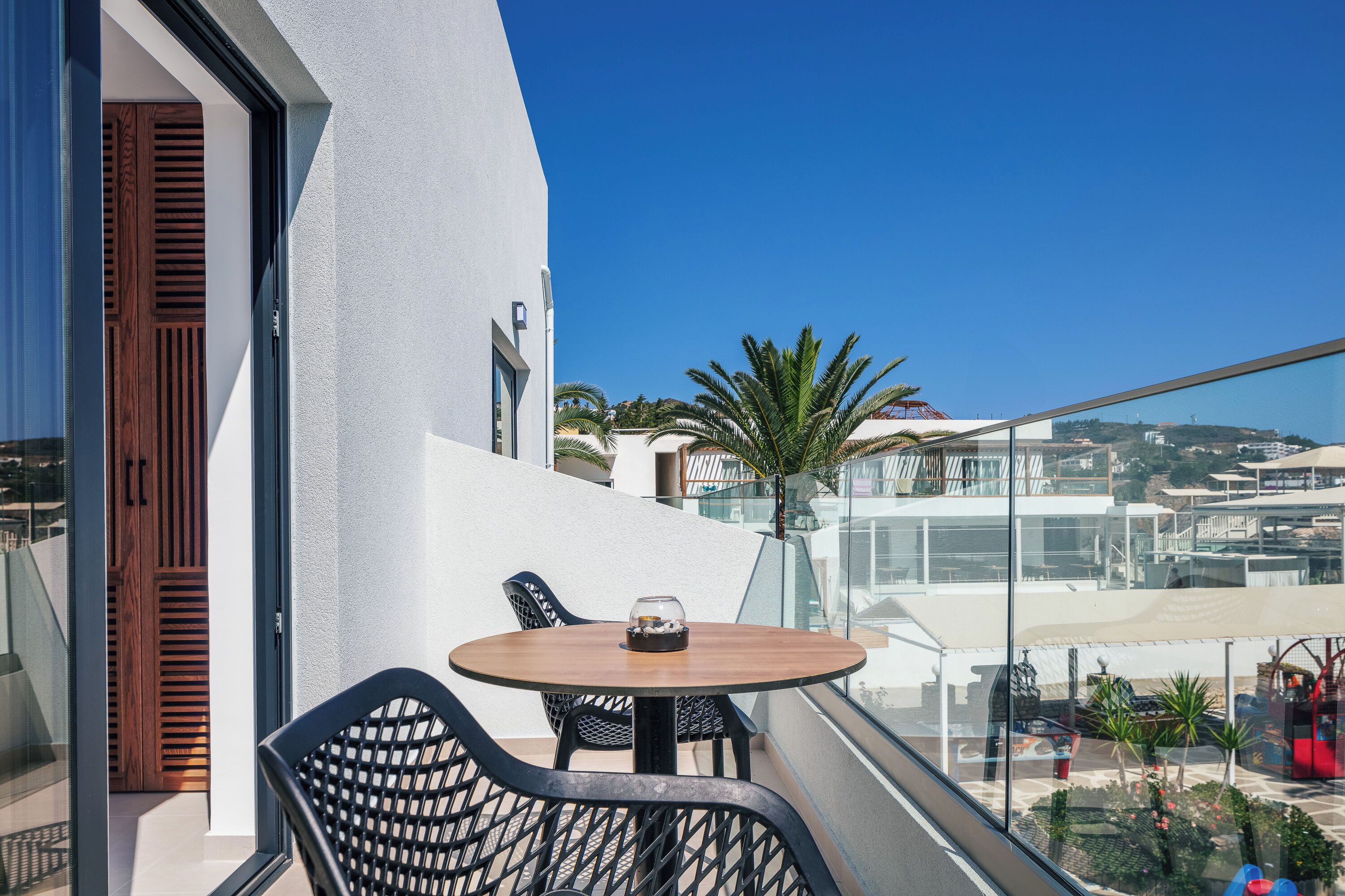 A balcony with a round table and chairs, a wooden door, and a view of the cityscape.