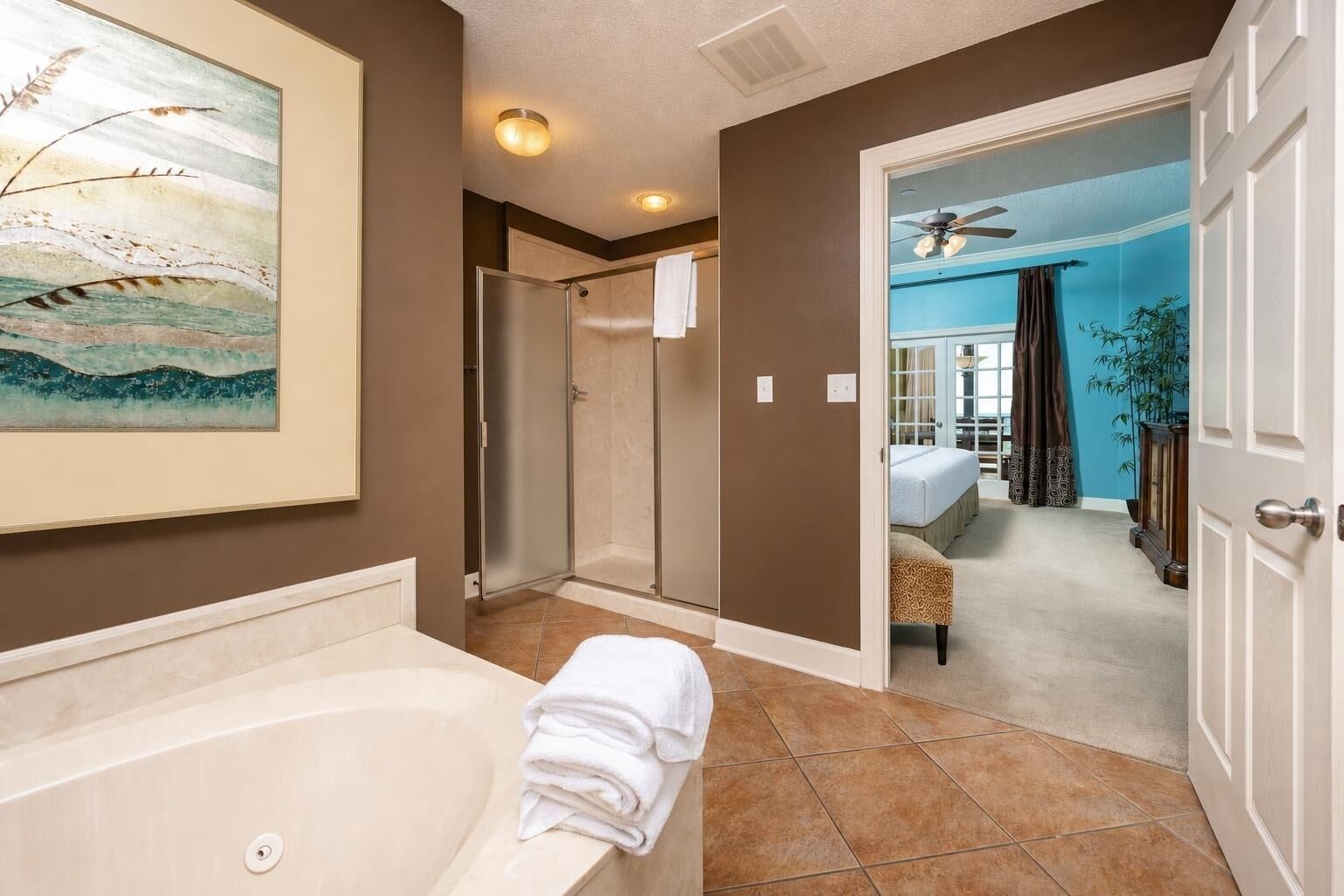 A bathroom with a bathtub, a shower, and a toilet. There is a painting on the wall and a door leading to a bedroom.