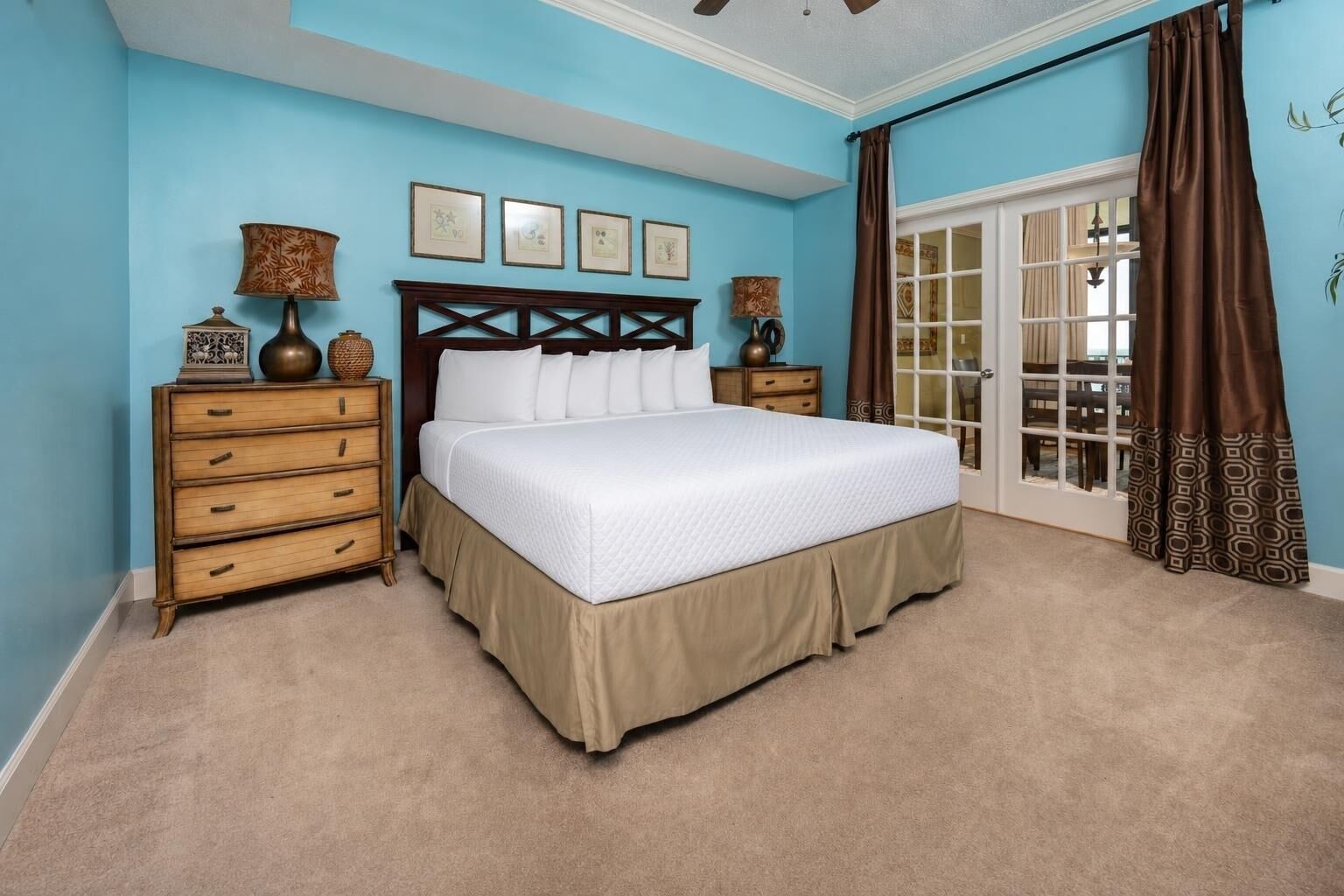 A bedroom with a bed, two nightstands, a dresser, and a large window with curtains.
