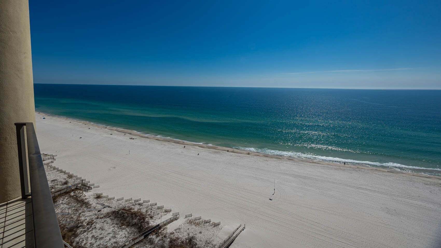 A beach view from a balcony with a clear sky, sandy beach, and ocean.