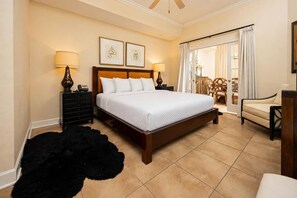 A hotel room with a large bed, a black furry rug, a wooden nightstand, two wall-mounted lamps, and a chair. - The Oasis 2404 Formerly Phoenix West Ii 2404 3 Bedroom Condo (Orange Beach)