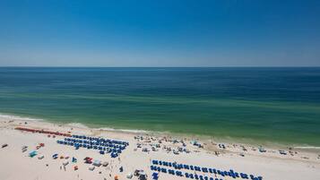 A beach with rows of blue umbrellas and sun loungers, a clear sky, and calm ocean waters.