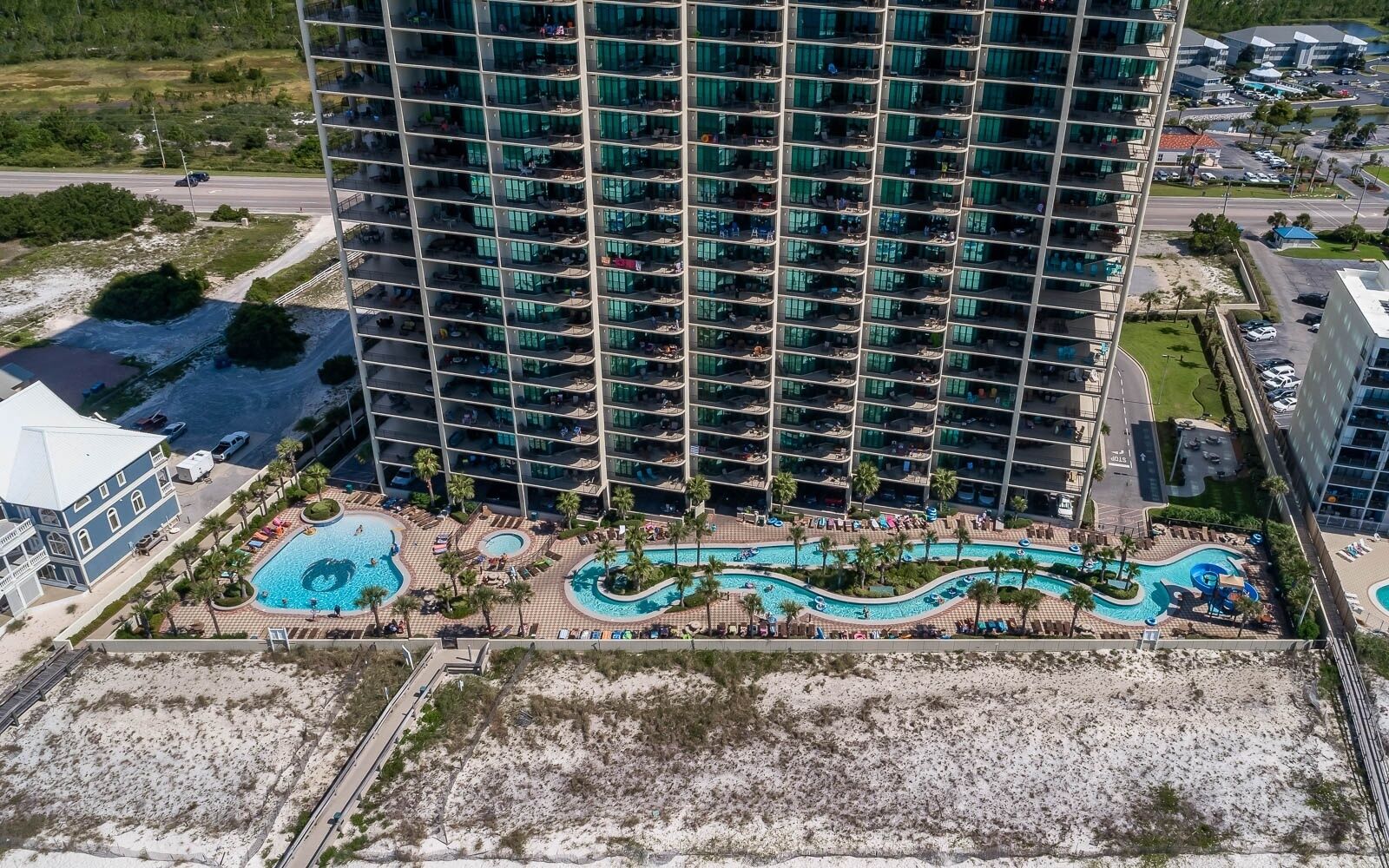 A high-rise hotel with multiple balconies, a swimming pool area, and a beach.
