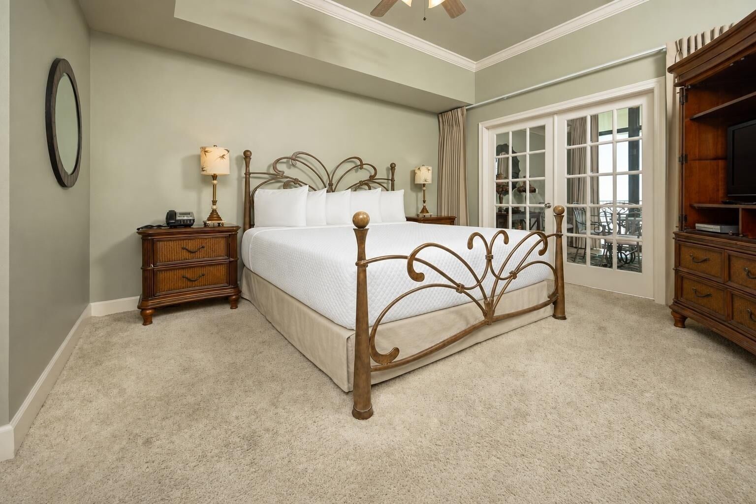 A bedroom with a bed, bedside tables, a dresser, a mirror, and a view through a glass door.