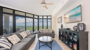 A living room with a sofa, a coffee table, a ceiling fan, a TV, and a bookshelf. - The Oasis 1815 Formerly Phoenix West Ii 1815 3 Bedroom Condo (Orange Beach)