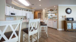 A kitchen with white cabinets, a microwave, a refrigerator, and a dining area with white chairs. - Phoenix West 2407 3 Bedroom Condo (Orange Beach)
