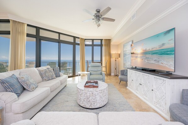 Ein geräumiges Wohnzimmer mit großem Fenster, Deckenventilator, Flachbildfernseher und Meerblick.