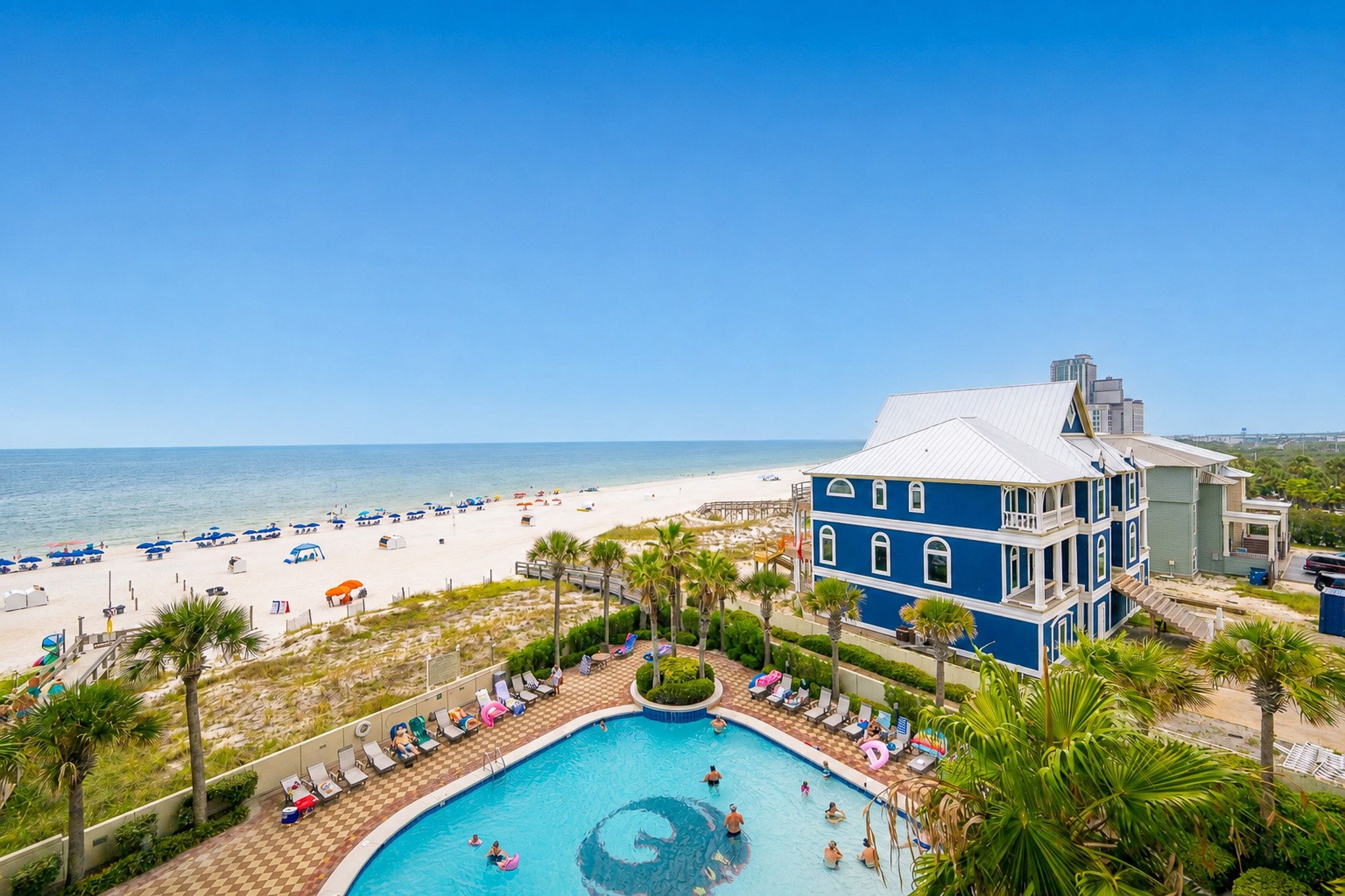 Een resort met een zwembad, strand en een groot blauw gebouw.