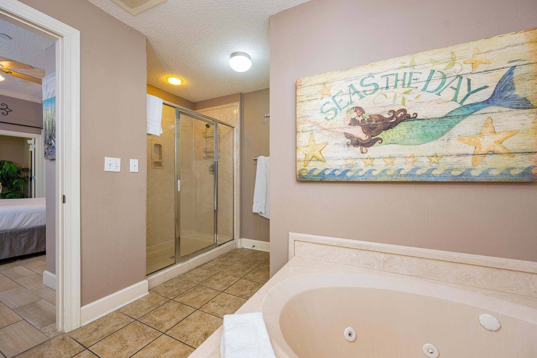 A bathroom with a large bathtub, a glass shower enclosure, and a wall mural.