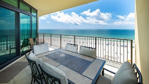 A balcony with a view of the beach and ocean, furnished with a table and chairs. - Phoenix West 702 3 Bedroom Condo (Orange Beach)