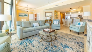 A living room with a sofa, armchairs, a coffee table, and a kitchen area with a bar. - Phoenix West 702 3 Bedroom Condo (Orange Beach)