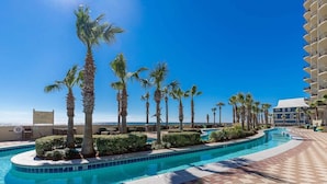 A swimming pool with palm trees, a clear sky, and a building with balconies. - Phoenix West 702 3 Bedroom Condo (Orange Beach)